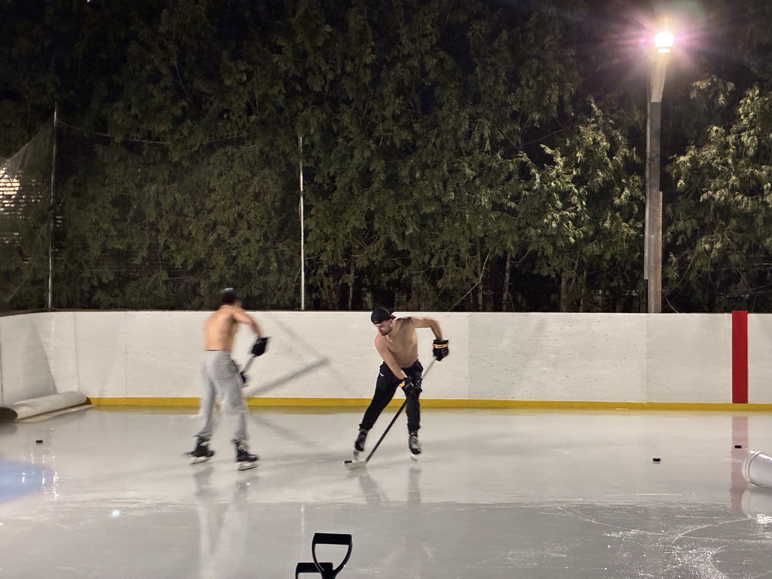 Two players in a shinny game, one carrying the puck out of the corner